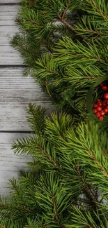 Green pine branches with red berries on a rustic wooden background.