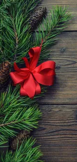 Festive mobile wallpaper with pine branches and red ribbon on wooden background.