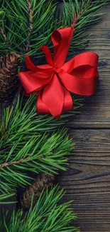 Pine branch with red bow on rustic wood background.