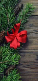 Festive wallpaper with pine branches and red bow on rustic wood.