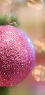 Pink glittery Christmas ornament with blurred festive lights.