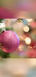 Pink Christmas ornament with bokeh effect on tree branch.