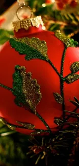 Red Christmas ornament adorned with green leaves on a tree.