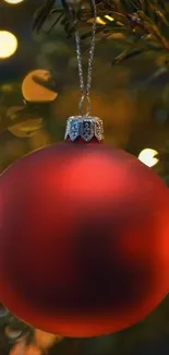 A red Christmas ornament hanging with glowing lights in the background.