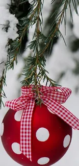 Red ornament with polka dots and ribbon in snowy pine branch.