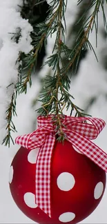 Red polka-dotted ornament hanging from snowy pine branch.