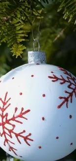 White Christmas ornament with red snowflakes on pine branch.