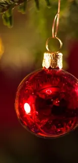 A vibrant red Christmas ornament hanging on a tree branch with a festive glow.