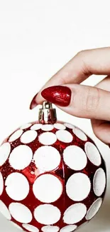 Hand holding red and white polka dot ornament, festive wallpaper design.