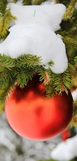 Red Christmas ornament in snowy pine branches.