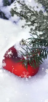 Red Christmas ornament in snow with pine branches and snowflakes.