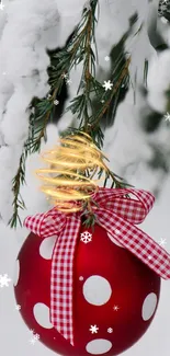 Christmas ornament with red ribbon on snow-covered pine branches.