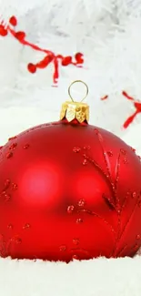 Red Christmas ornament against snowy white background.