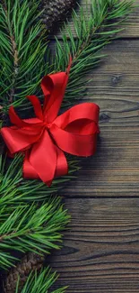 Red ribbon on pine branches with wooden background, ideal for festive wallpaper.