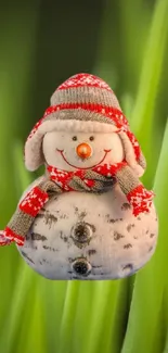 Cute snowman with red hat on green grass field, close-up view.