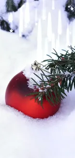 Red ornament in snow with evergreen branch.