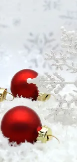 Red Christmas ornaments in snow with white snowflakes.