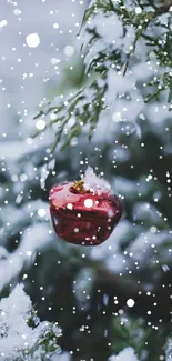 A red Christmas ornament hangs on a snowy tree branch, surrounded by falling snow.