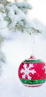 Festive red ornament on a snowy evergreen branch, perfect for holiday wallpaper.