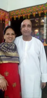 Smiling couple in traditional attire with festive backdrop.