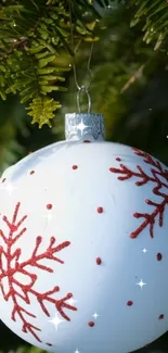 White ornament with red snowflakes hanging on a pine branch.