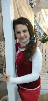 Woman in festive red dress standing near white column indoors.