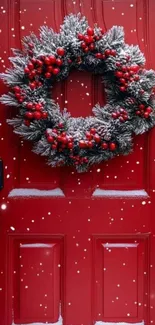 A festive wreath with berries on a red door, dusted with snow.