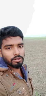 Man taking a selfie in a tranquil field with a sunrise backdrop.