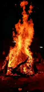 A large bonfire blazing warmly at night under a dark sky.