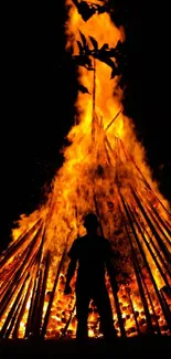 Silhouette against a large blazing bonfire at night.