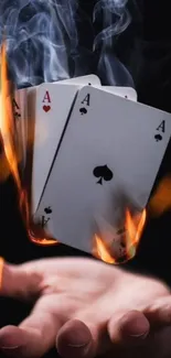 Playing cards on fire with smoke and hand underneath.