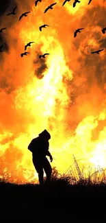 Silhouette against a large blazing fire with birds flying above.