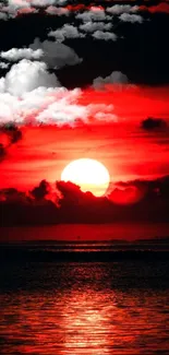 Fiery sunset over ocean with red sky and clouds.