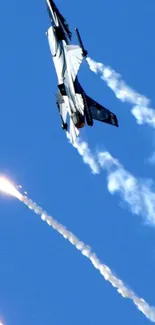 Fighter jet soaring in a vibrant blue sky with contrails and flares.