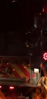 A firetruck with glowing red lights at night with flames below.