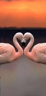 Two flamingos form a heart against a vibrant sunset.