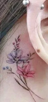 Delicate floral tattoo on ear with pink and purple hues.