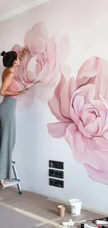 Woman painting a large pink floral mural on a wall.