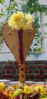 Snake deity with yellow flower garland against a natural backdrop.