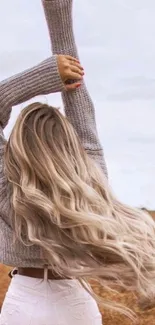 Woman with flowing hair in an autumn field wearing a cozy sweater.