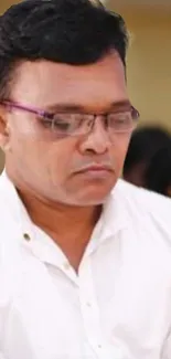 Man wearing glasses in a white shirt, looking focused.