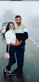 A couple stands together on a foggy road, creating a romantic roadside scene.