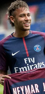 Football player smiling and holding a jersey in a stadium.