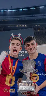 Two football players celebrating with a trophy in a stadium.