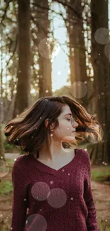 Woman in burgundy sweater standing in a serene forest with bokeh lights.