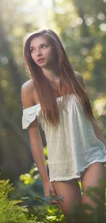 Young woman in white dress standing in sunlit forest.