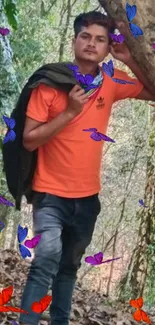 Man in orange shirt standing in forest setting with lush green trees.