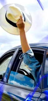 Arm holding hat out of car window with blue sky and accents.