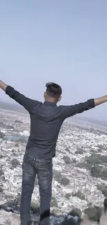 Person standing with open arms on a mountain, facing a scenic landscape view.