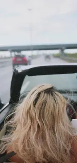 Woman enjoying convertible ride with arm raised on open highway.